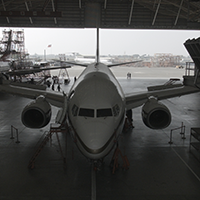 Front view of a commercial airplane parked inside a large maintenance hangar.